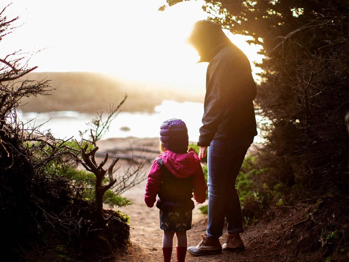 A parent and young child on a coastal trail at sunset