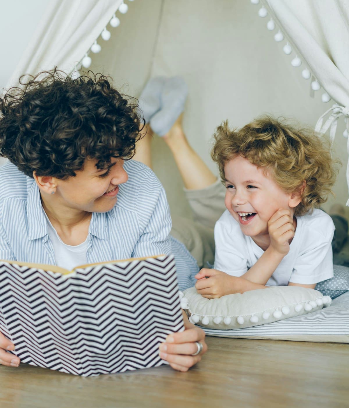 An adult and a child laughing together while reading
