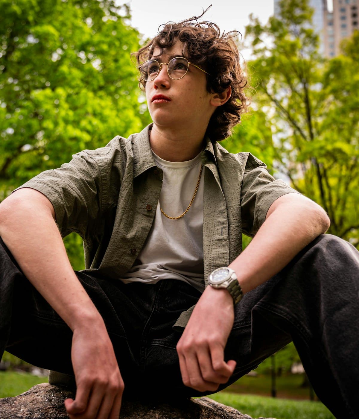 A young man sitting outdoors, looking up thoughtfully