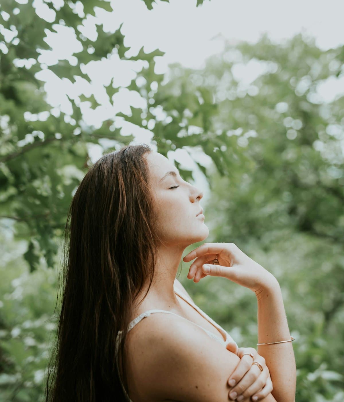 A woman with her eyes closed, breathing among trees